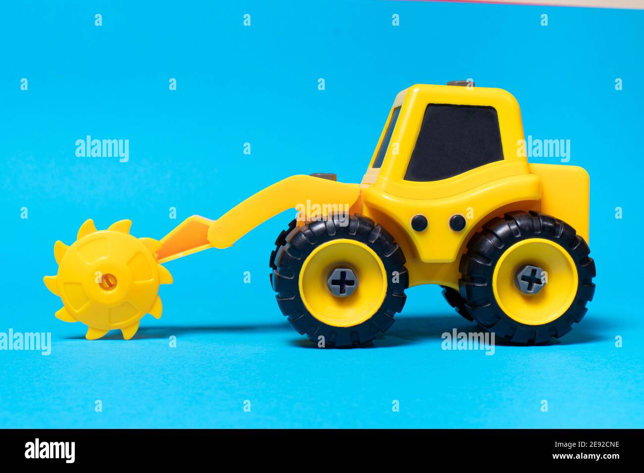 Trattore giallo giocattolo con ugello per sega circolare per legno su sfondo blu. Apparecchi per macchine da costruzione per il negozio di giocattoli. Foto Stock