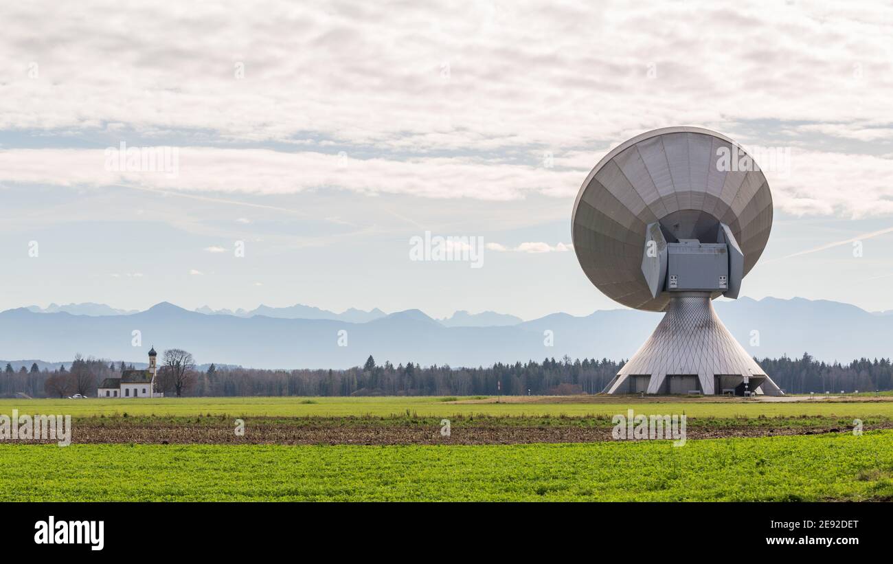 Raiding, Germania - 13 novembre 2020: Vista sul retro di un'antenna parabolica. In lontananza la sagoma delle montagne (alpi) e una chiesa. Foto Stock
