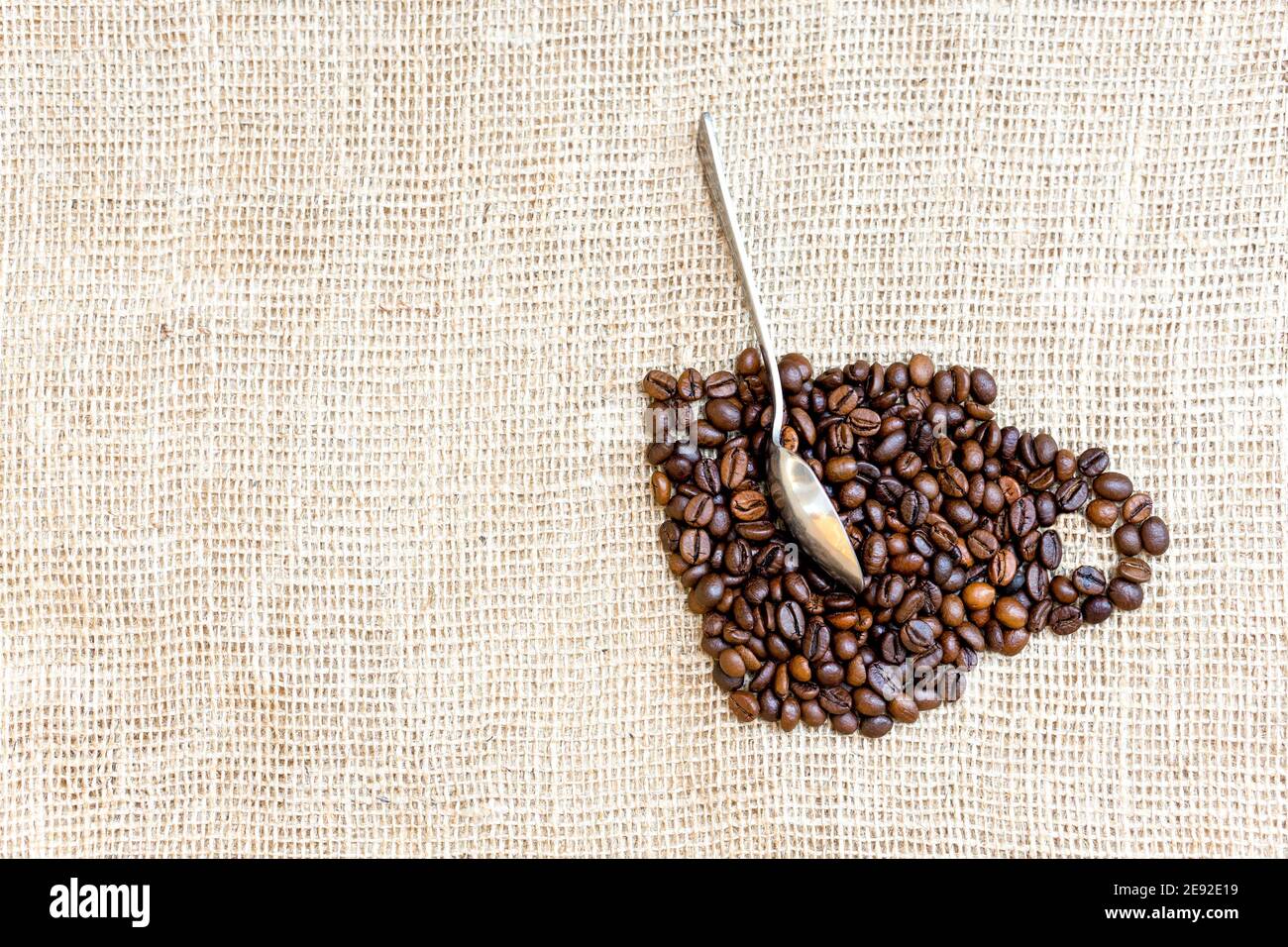 Disposizione creativa di chicchi di caffè tostati nella forma di una tazza con un cucchiaio su un panno Foto Stock