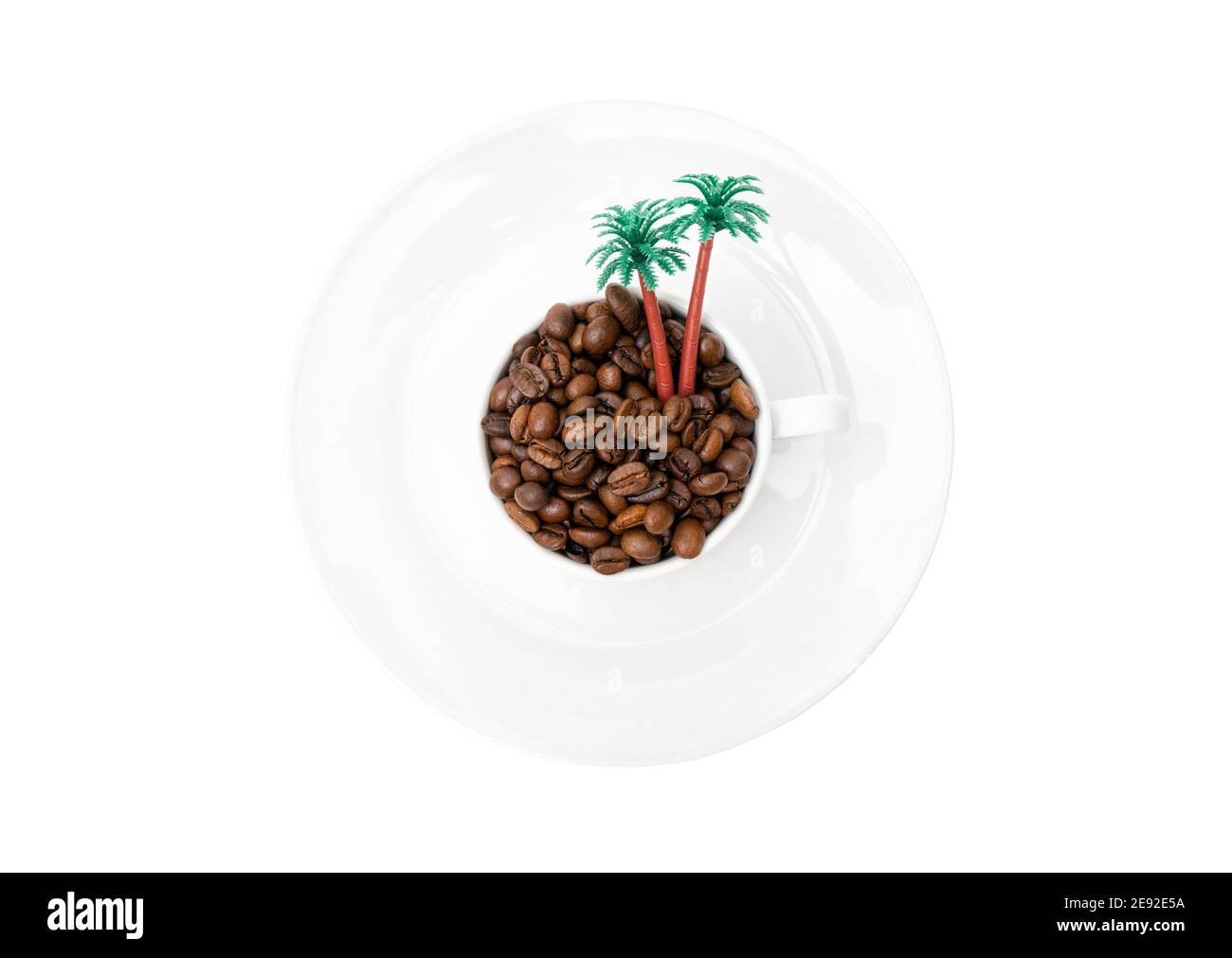 Vista dall'alto di una piccola isola giocattolo composta da chicchi di caffè tostati e palme giocattolo in una tazza di caffè su un piatto bianco isolato su sfondo bianco. Foto Stock