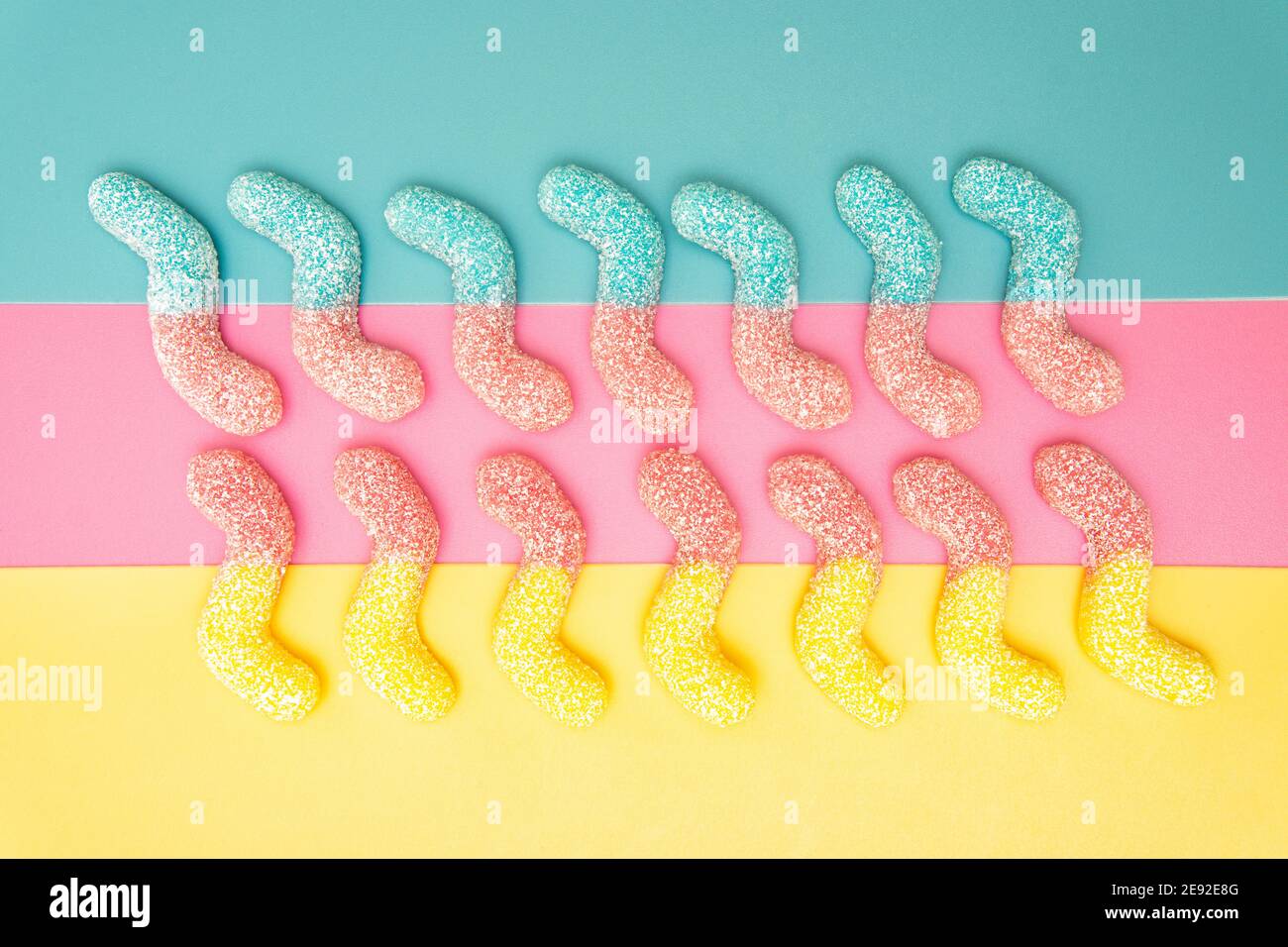 Due file di vermi gommoso ricoperti di zucchero multicolore su un sfondo brillante Foto Stock
