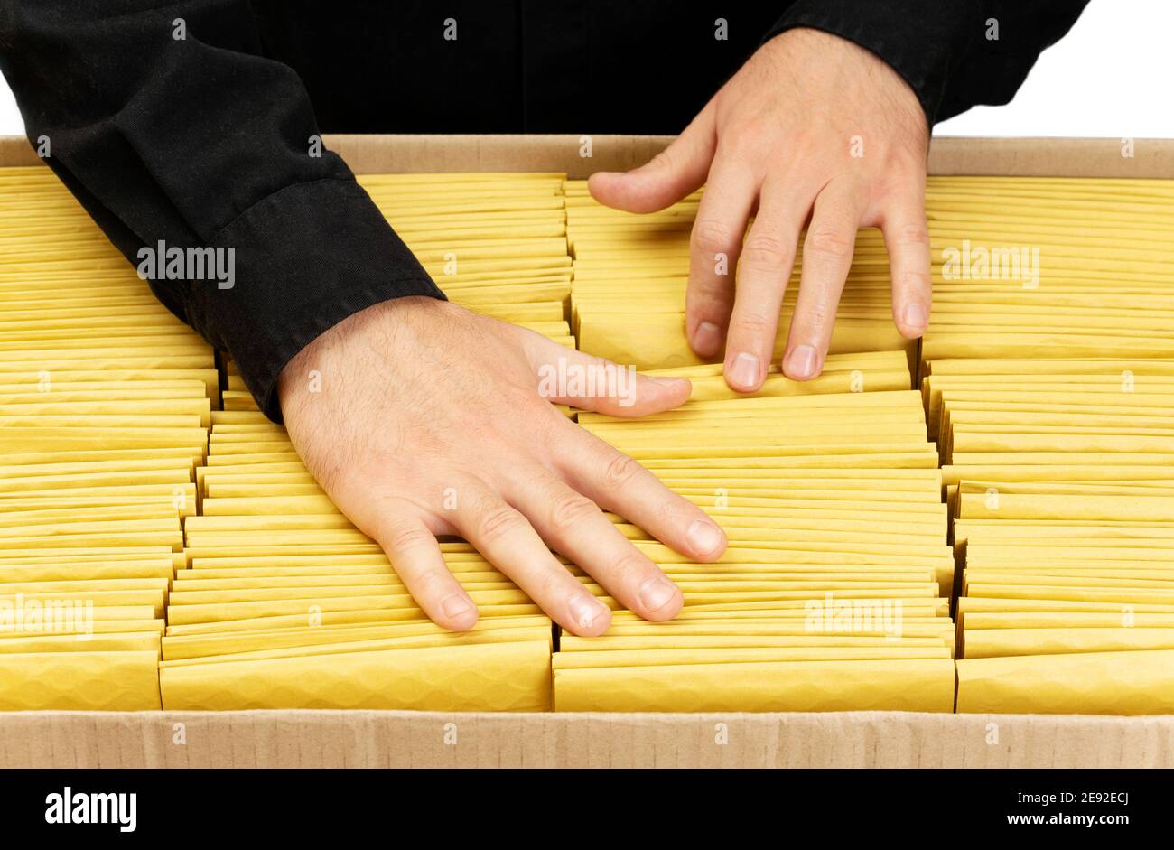 Uomo in nero uniforme contando buste gialle imbottite in una grande scatola di cartone. Foto Stock