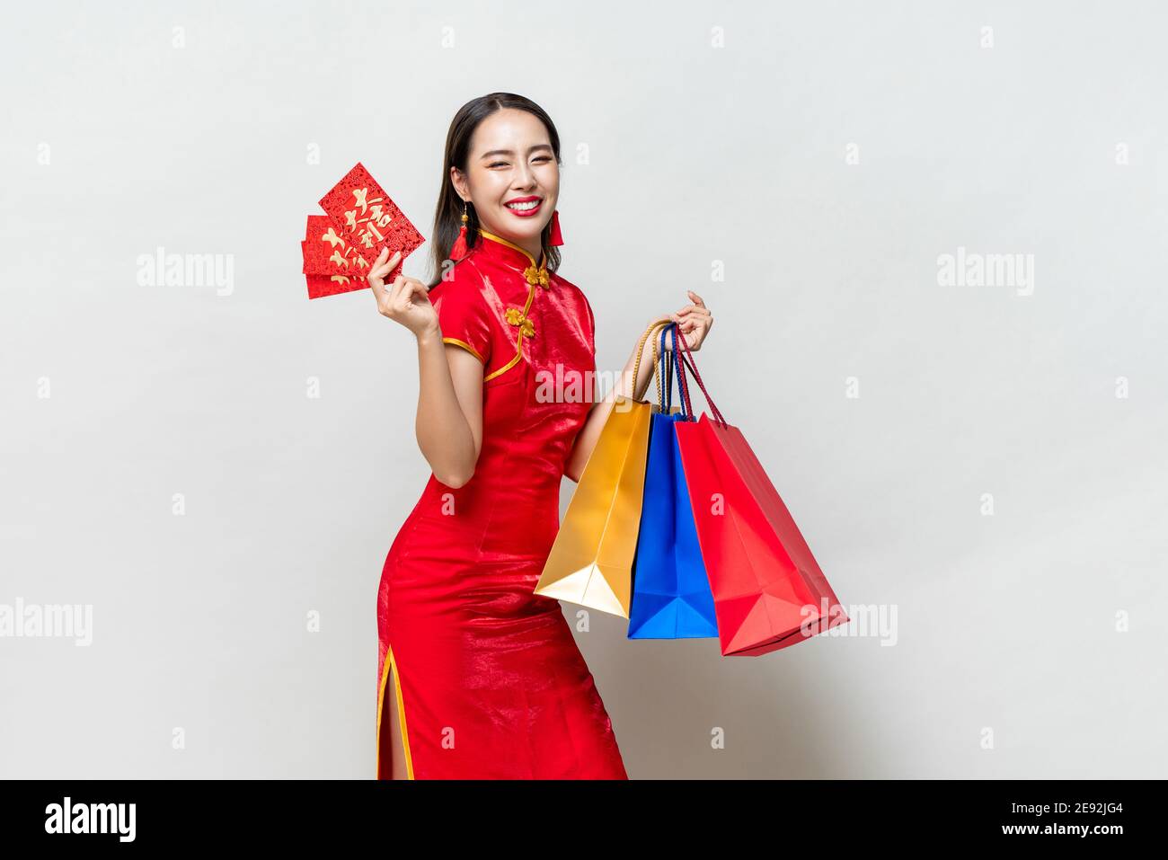 Donna asiatica in abito tradizionale qipao che tiene borse e buste rosse in isolato grigio chiaro sfondo studio per il concetto cinese di shopping di nuovo anno, Foto Stock