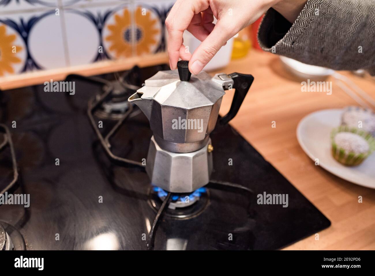 La mano circa per sollevare il coperchio di una caffettiera di ferro da stiro posizionata sul fuoco della cucina. Preparazione del caffè Foto Stock
