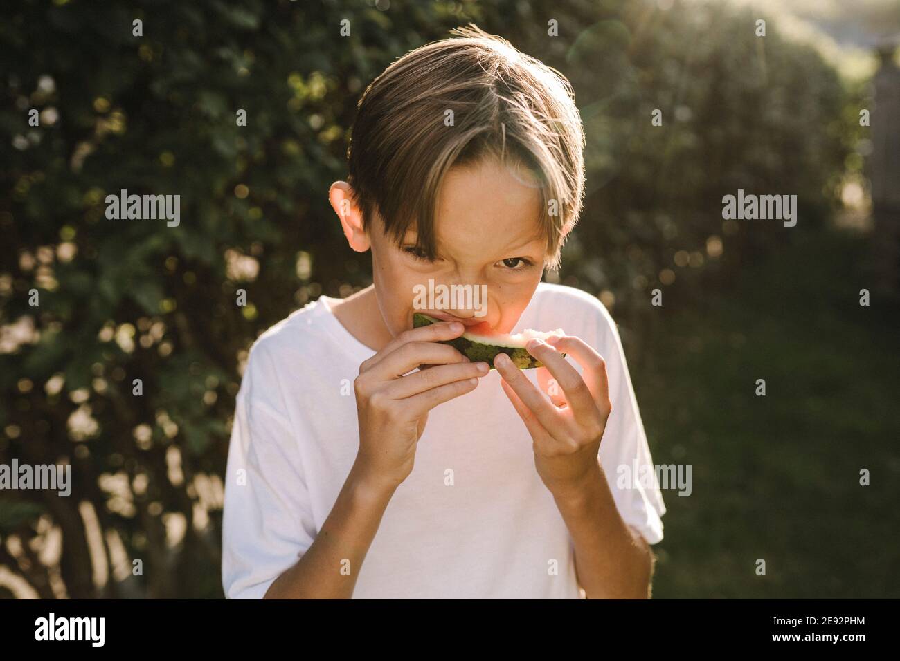 Ragazzo che mangia l'anguria mentre si trova nel cortile posteriore Foto Stock