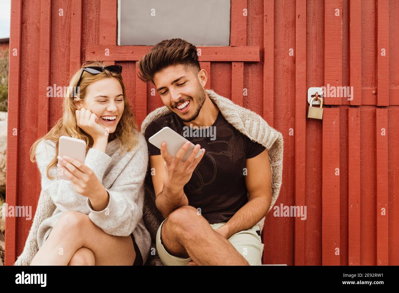 Gli amici ridono mentre usano il telefono cellulare contro il cottage Foto Stock