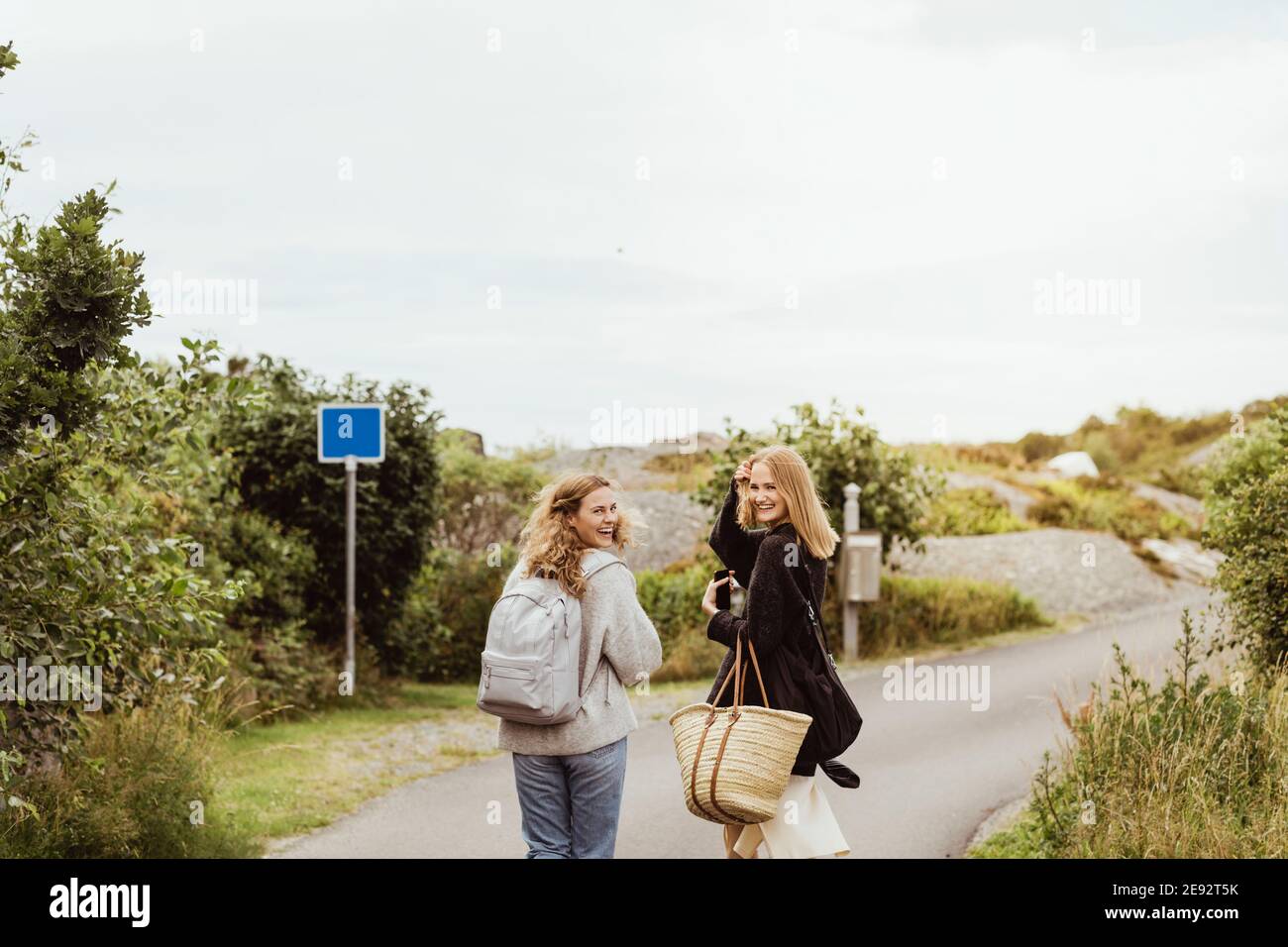 Sorridi le amiche che guardano le spalle mentre camminano sulla strada durante le vacanze estive Foto Stock Sorridi le amiche che guardano le spalle mentre camminano sulla strada durante le vacanze estive Foto Stock