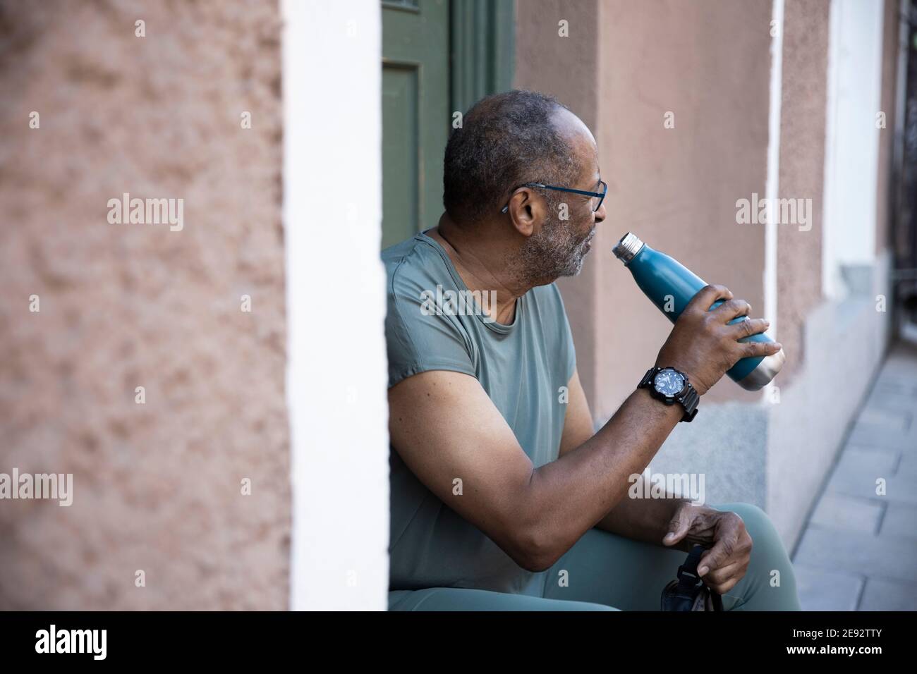 Uomo anziano assetato con bottiglia alla porta di casa Foto Stock