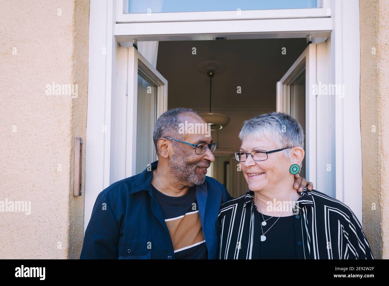Uomo anziano con braccio intorno in piedi da donna anziana a. casa Foto Stock