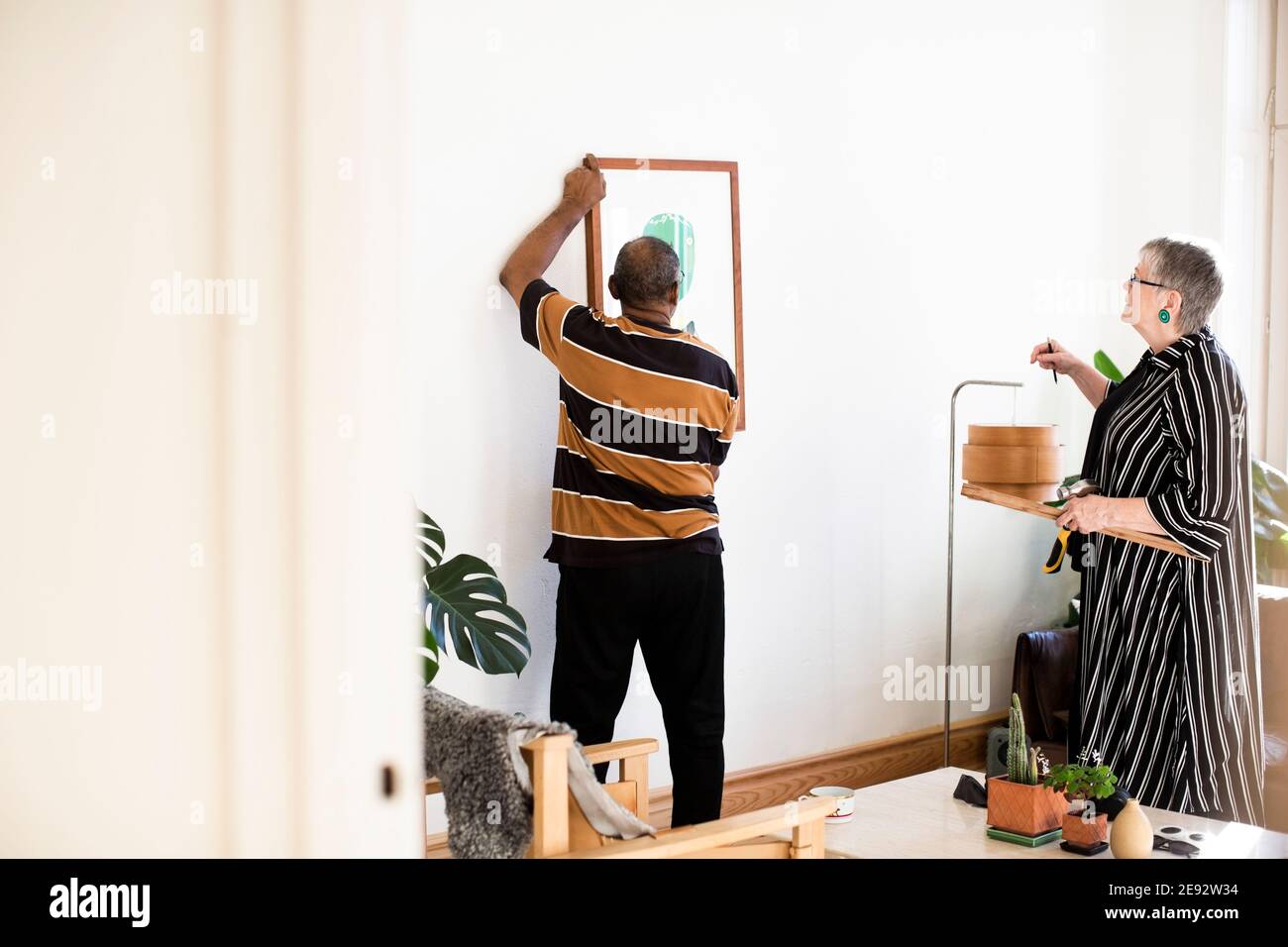 Uomo anziano che regola la pittura mentre si sta contro la donna in vita camera Foto Stock