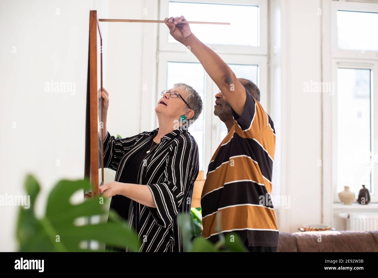 Coppia eterosessuale che misura la pittura mentre appende sul muro in vita camera Foto Stock