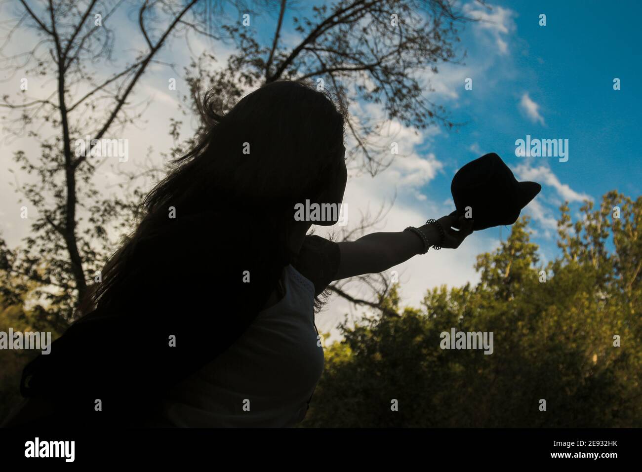 Basso angolo shot di giovane ragazza in silhouette che la solleva Paglia hat.Nice cielo blu con le nuvole Foto Stock
