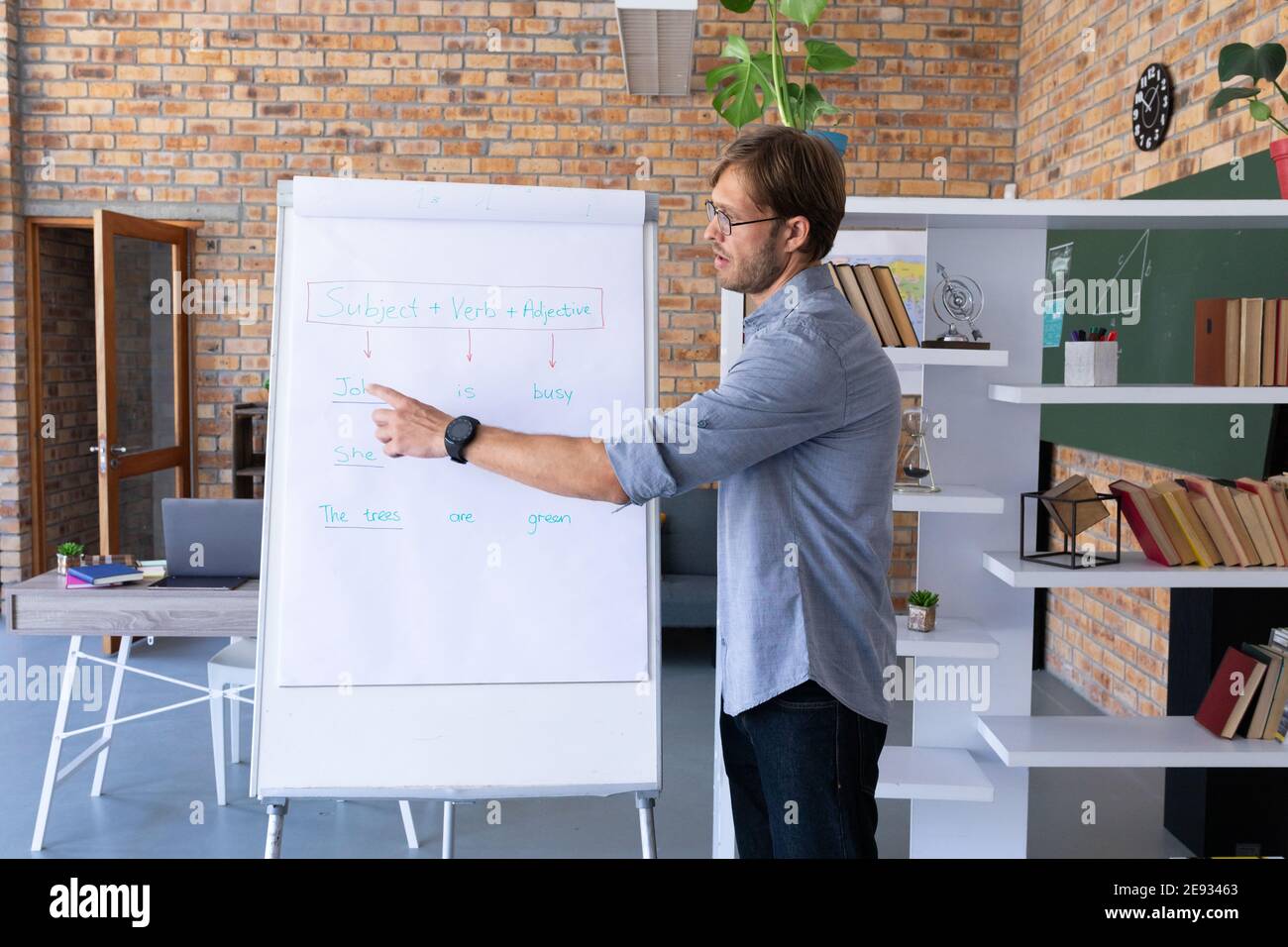 Insegnante di inglese maschio caucasico che dà la lezione in linea che sta parlando usando cuscinetto a cavalletto Foto Stock