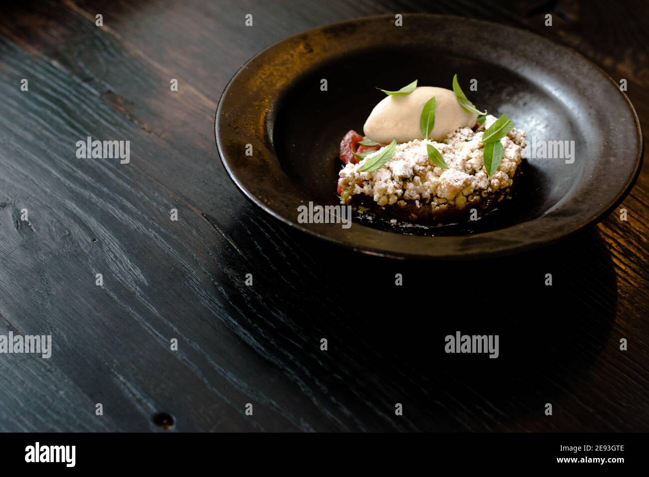 Piatto di sorbetto e torta di rabarbaro coperto con foglie di menta in un piatto nero su un tavolo di legno in un ristorante Foto Stock
