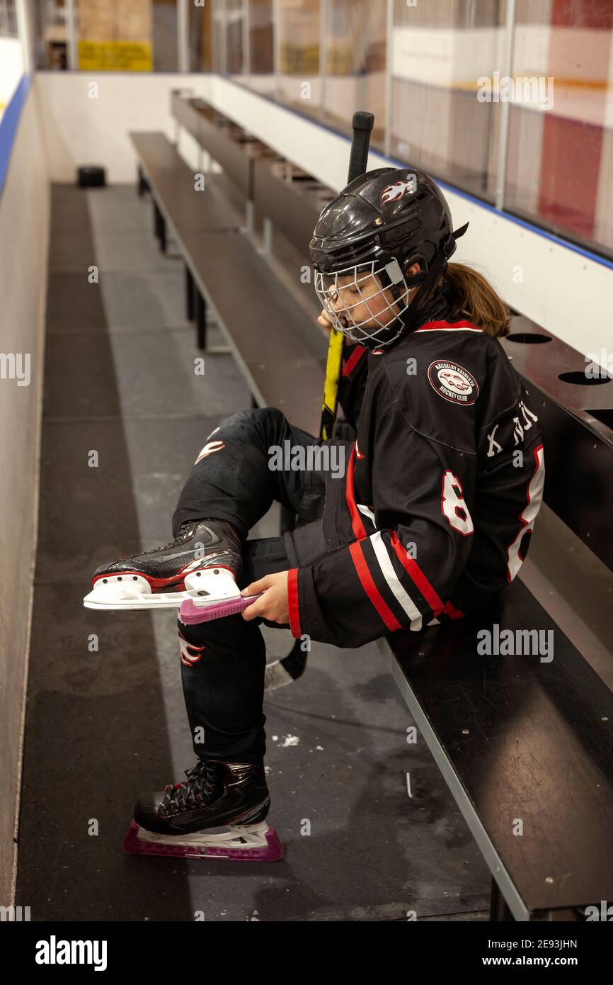 Ragazza giocatore di hockey mettere guardie su pattini di ghiaccio Foto Stock