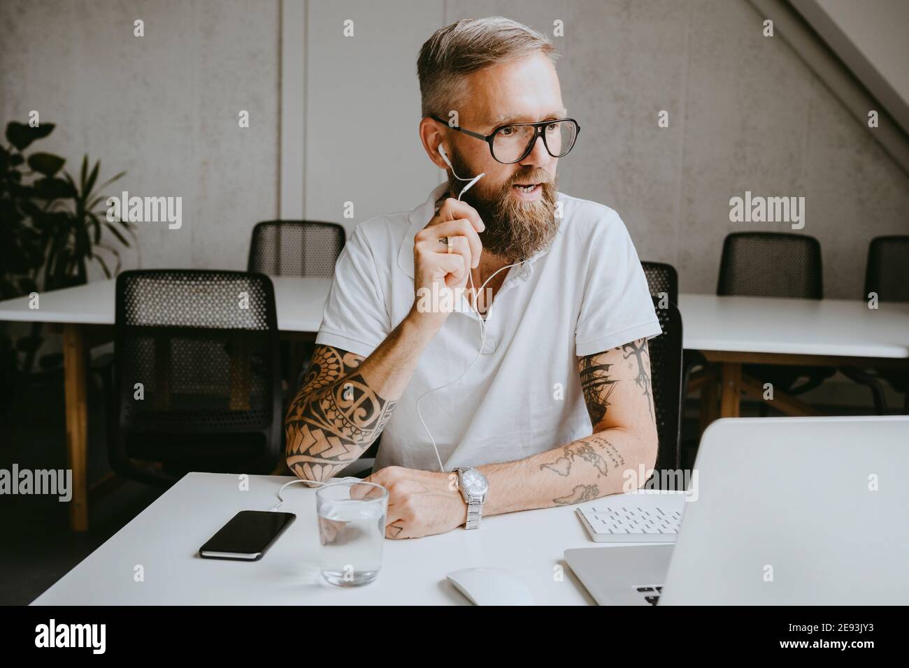 Uomo d'affari che parla con gli auricolari mentre lavora in ufficio Foto Stock