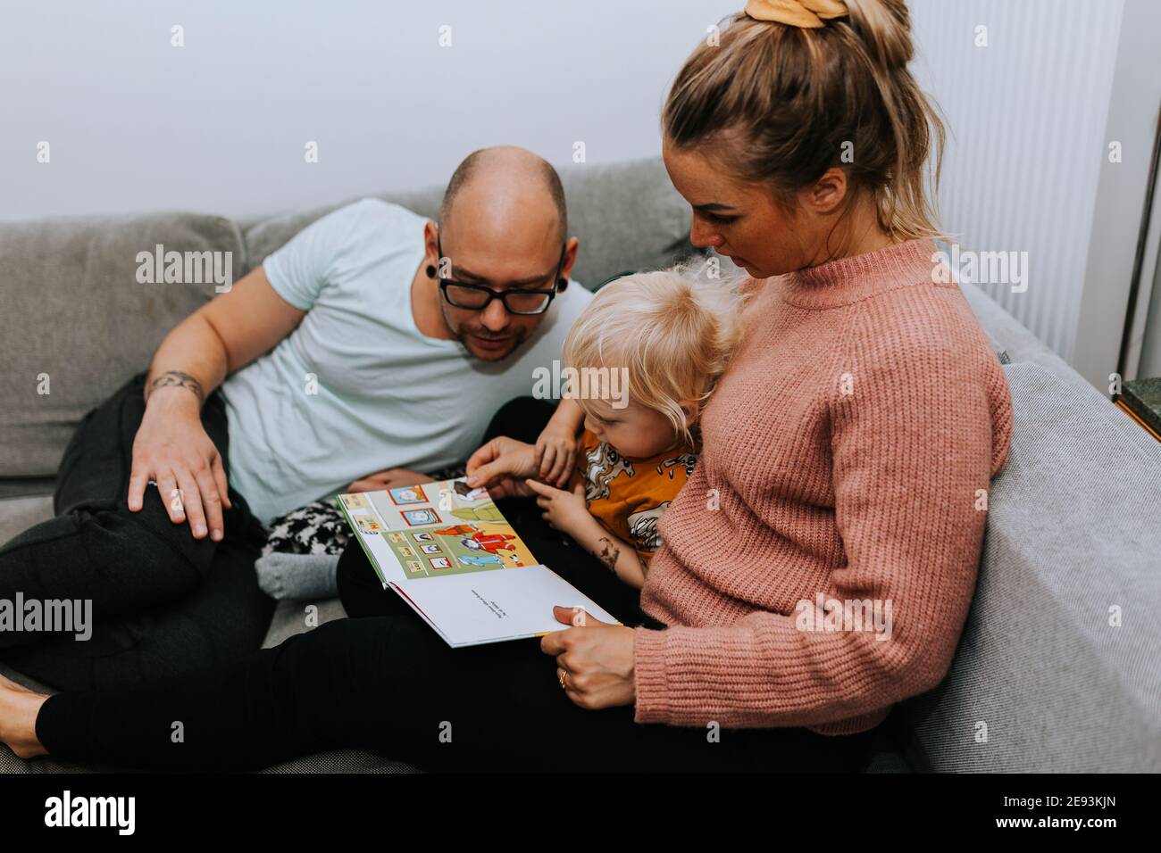 I genitori leggono il libro dei bambini sul divano Foto Stock