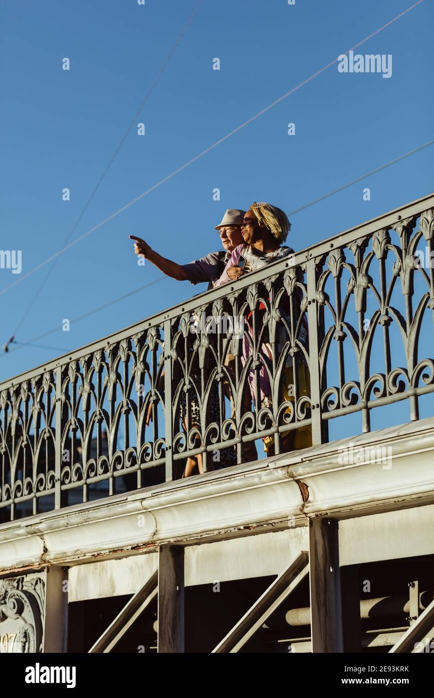 Uomo anziano che indica mentre si sta in piedi da donna sul ponte contro cielo blu Foto Stock