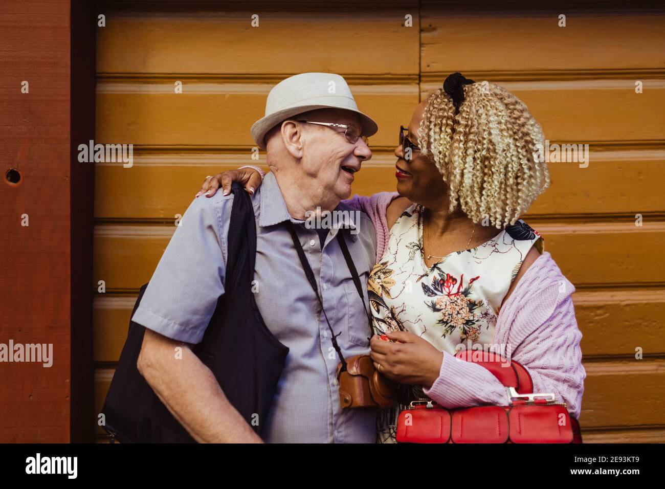 Sorridente coppia anziana con le braccia intorno contro il muro Foto Stock