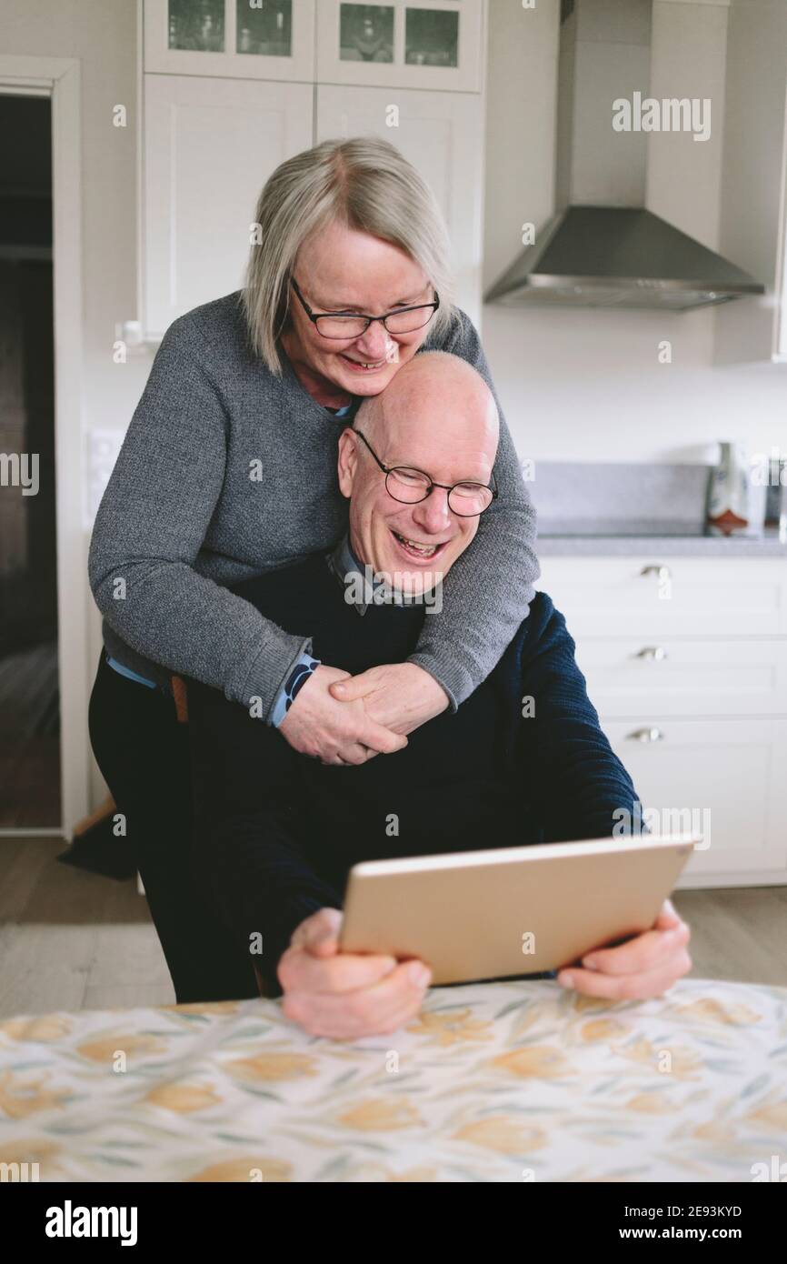 Una coppia sorridente che si è abbracciata e ha una chat video sul tablet a. tavolo da cucina Foto Stock