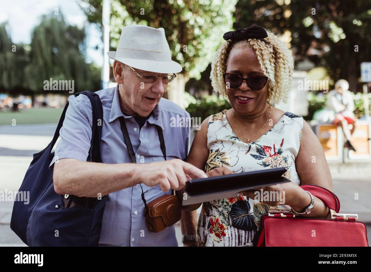 Sorridente coppia senior che utilizza il tablet digitale in strada durante il sole giorno Foto Stock