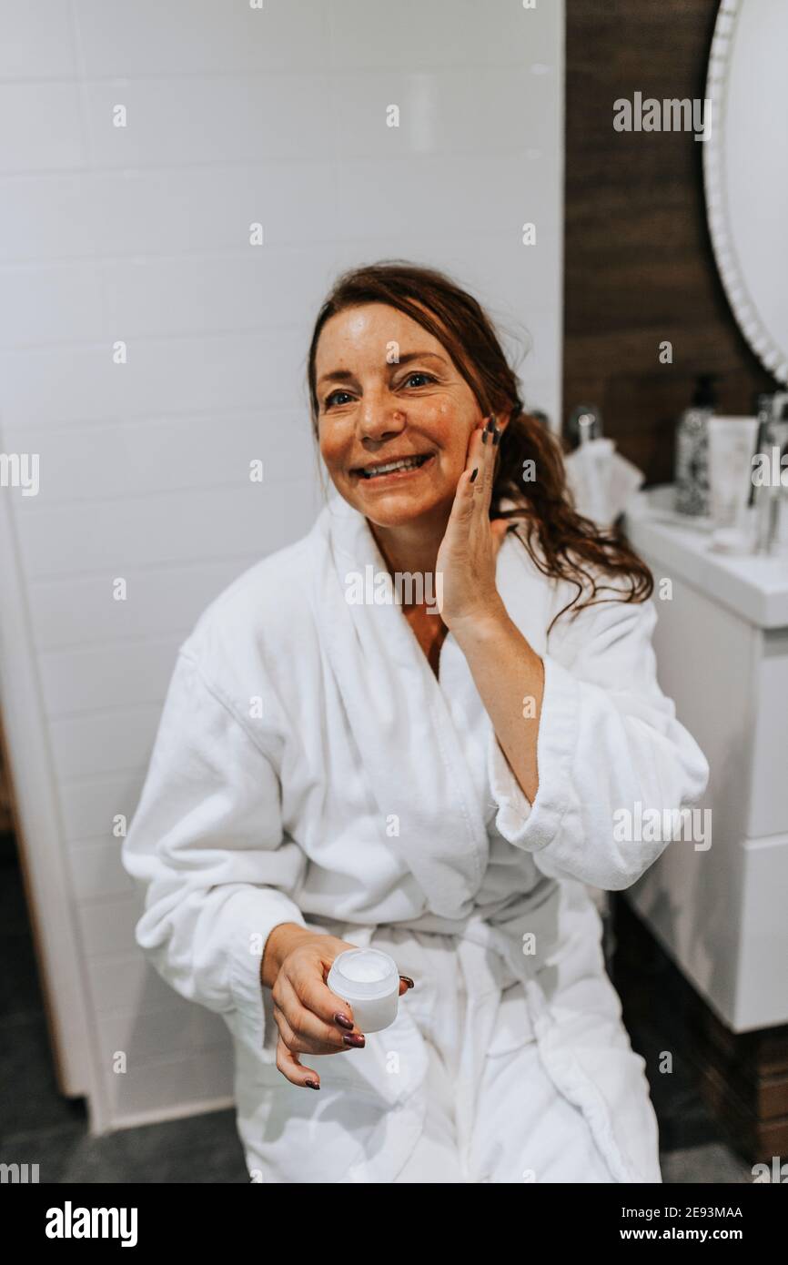 Donna di applicare una crema idratante sul suo viso Foto Stock