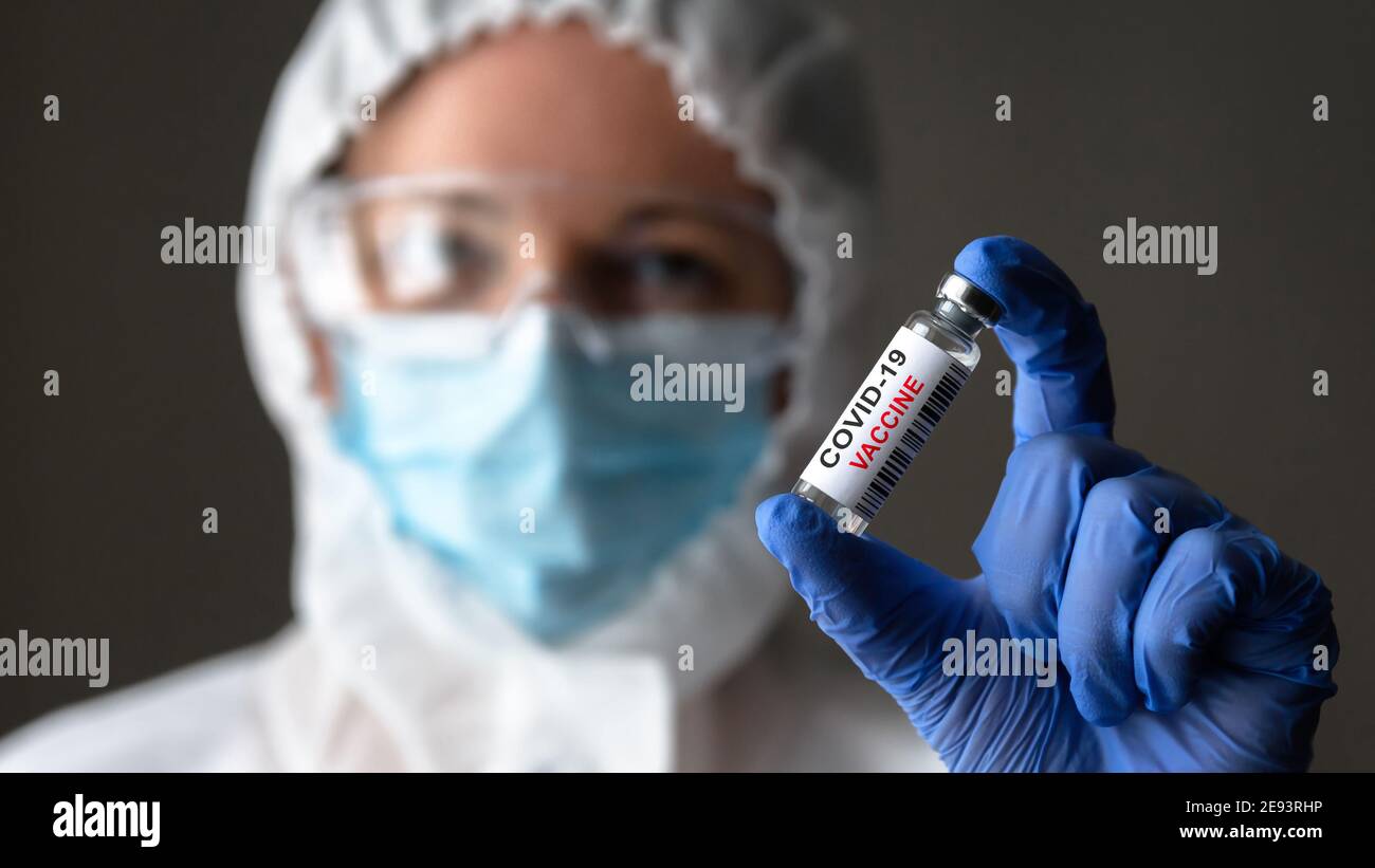Vaccino COVID-19 nelle mani del medico da vicino, infermiere in dispositivi medici di protezione individuale (DPI) contiene flacone con vaccino per la cura del coronavirus. Conce Foto Stock