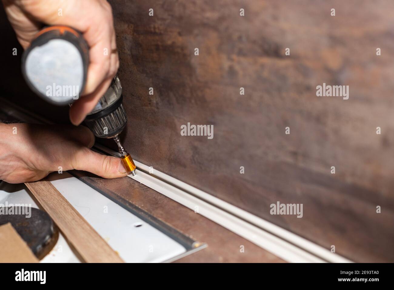 L'artigiano installa i battiscopa con un cacciavite sul piano di legno e sul grembiule da cucina. Riparazione e miglioramento dell'alloggiamento. Foto Stock