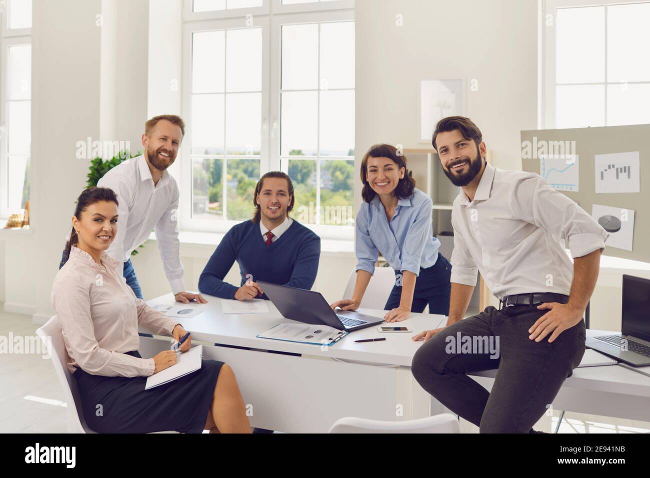 Gruppo di giovani uomini d'affari sorridenti seduti in ufficio e. guardare la fotocamera durante la discussione di avvio insieme Foto Stock