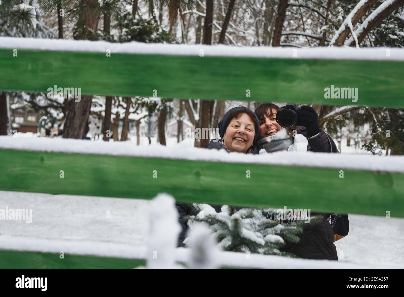 Felice madre con figlia che fa selfie foto in specchio con fotocamera professionale all'aperto nel parco invernale innevato Foto Stock
