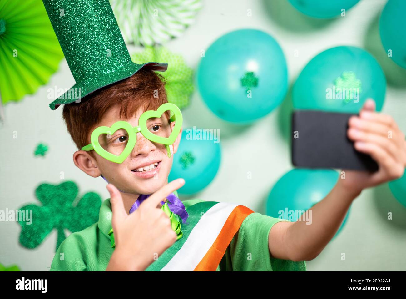 Bambino in videochiamata durante la festa di san Patrizio sul telefono cellulare e mostra lo sfondo decorato durante la videochiamata - concetto di fe distante Foto Stock