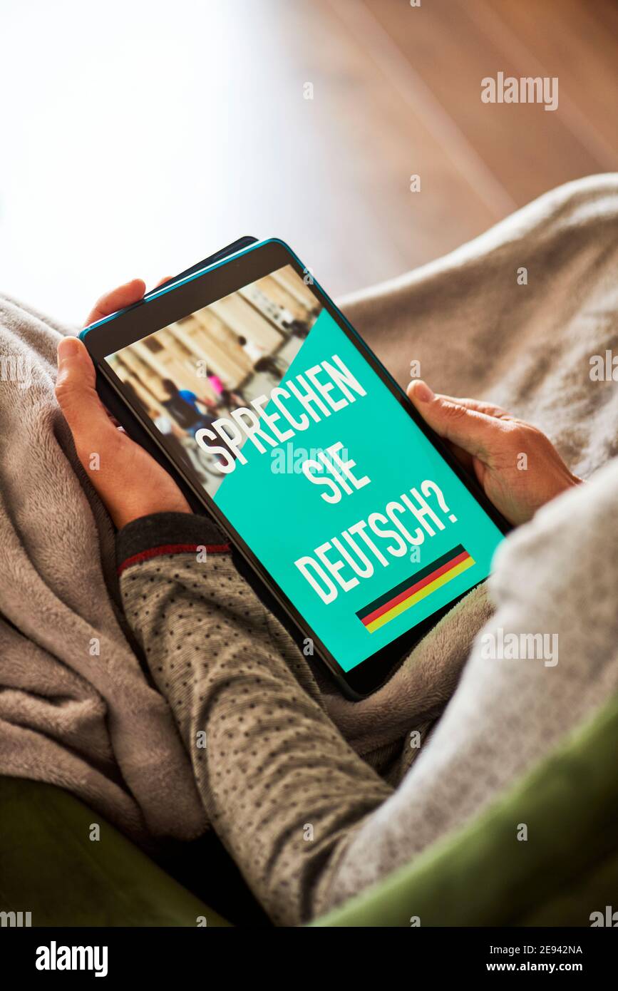 un giovane caucasico è seduto comodamente in un divano avvolto in una coperta grigia calda, e ha la sua tavoletta in mano, con il testo si parla Foto Stock