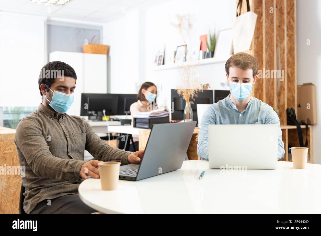 I colleghi si sono concentrati sui loro computer portatili e indossano maschere facciali di protezione. Lavorare in ufficio durante il concetto pandemico di Coronavirus. Foto Stock