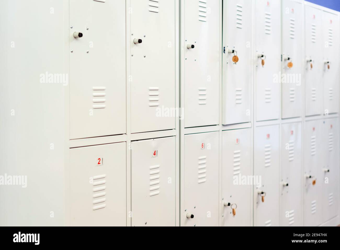 Una fila di armadietti scuola in metallo grigio con le chiavi nelle porte. Deposito ripostiglio in corridoio di istituto educativo Foto Stock