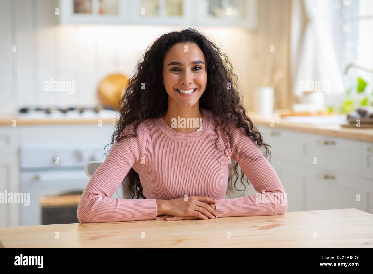 Ritratto di bella gioiosa giovane Signora seduta a Table in Cucina interna Foto Stock