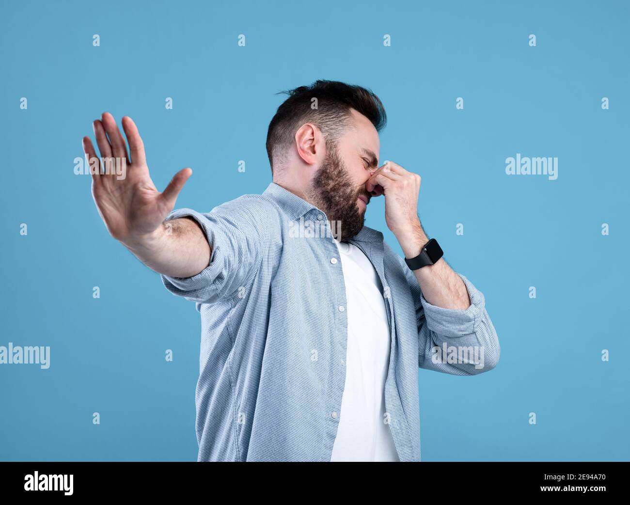Cattivo odore. Giovane ragazzo bearded che chiude il naso e mostra un gesto DI STOP, esprimendo disgusto su sfondo blu dello studio Foto Stock