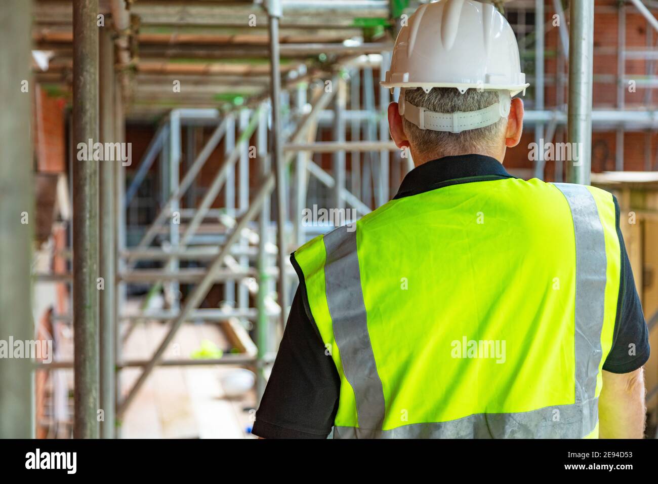 Vista posteriore del costruttore maschile lavoratori o costruttore su cantiere che indossa cappello e gilet hi-vis Foto Stock