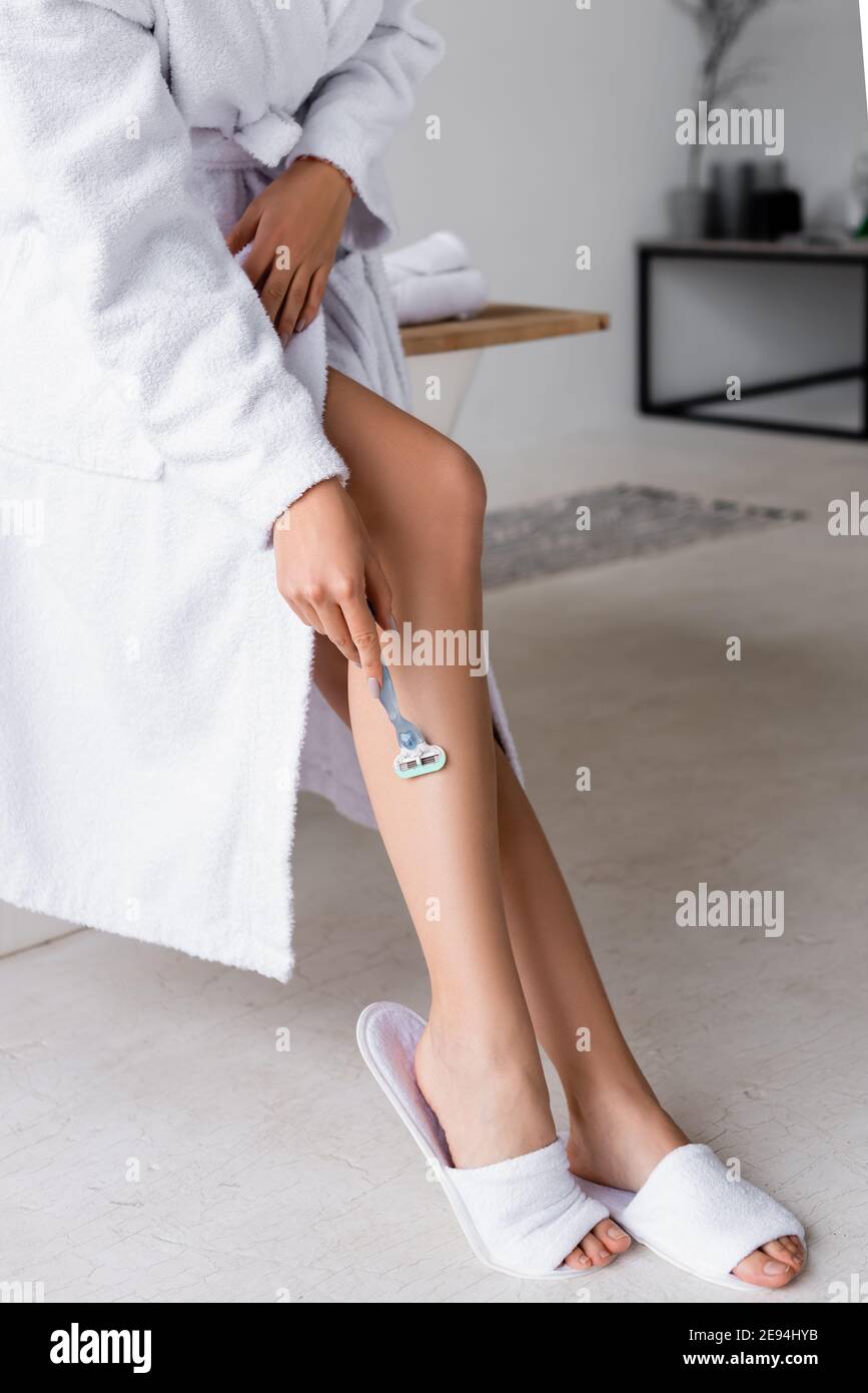 Vista dal taglio corto della donna in accappatoio e ciabatte con gamba di rasatura in bagno Foto Stock