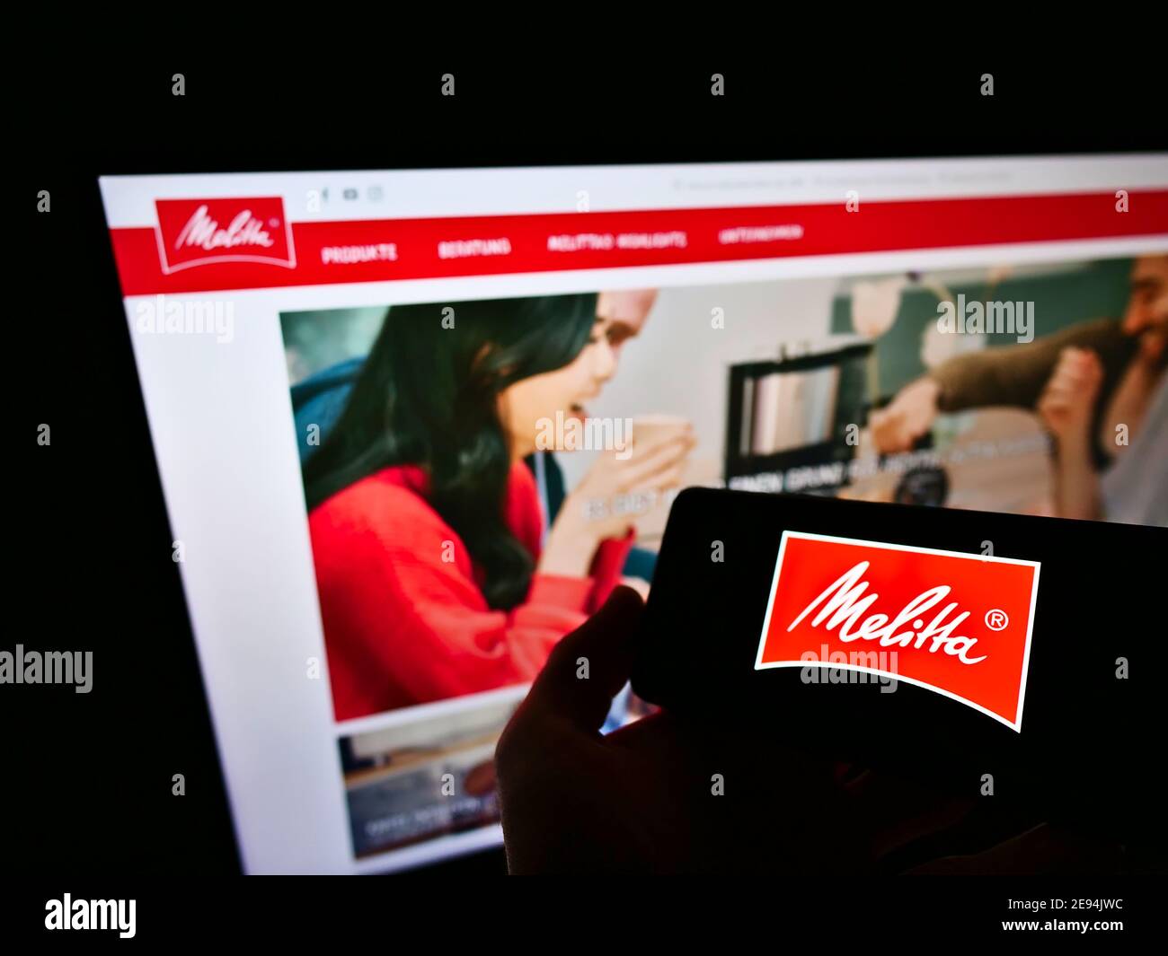 Persona che tiene il cellulare con il logo commerciale della società tedesca di caffè al dettaglio Melitta in esposizione davanti alla pagina web. Mettere a fuoco lo schermo dello smartphone. Foto Stock