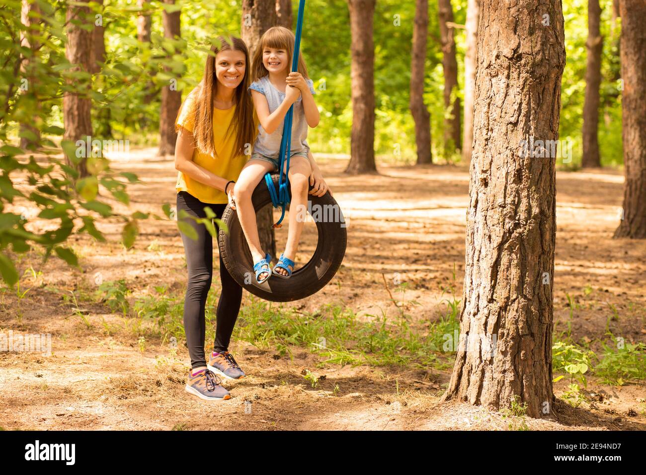 Felice mamma e figlia oscillano sulla ruota con sfondo estate natura. Tempo di famiglia attivo insieme Foto Stock