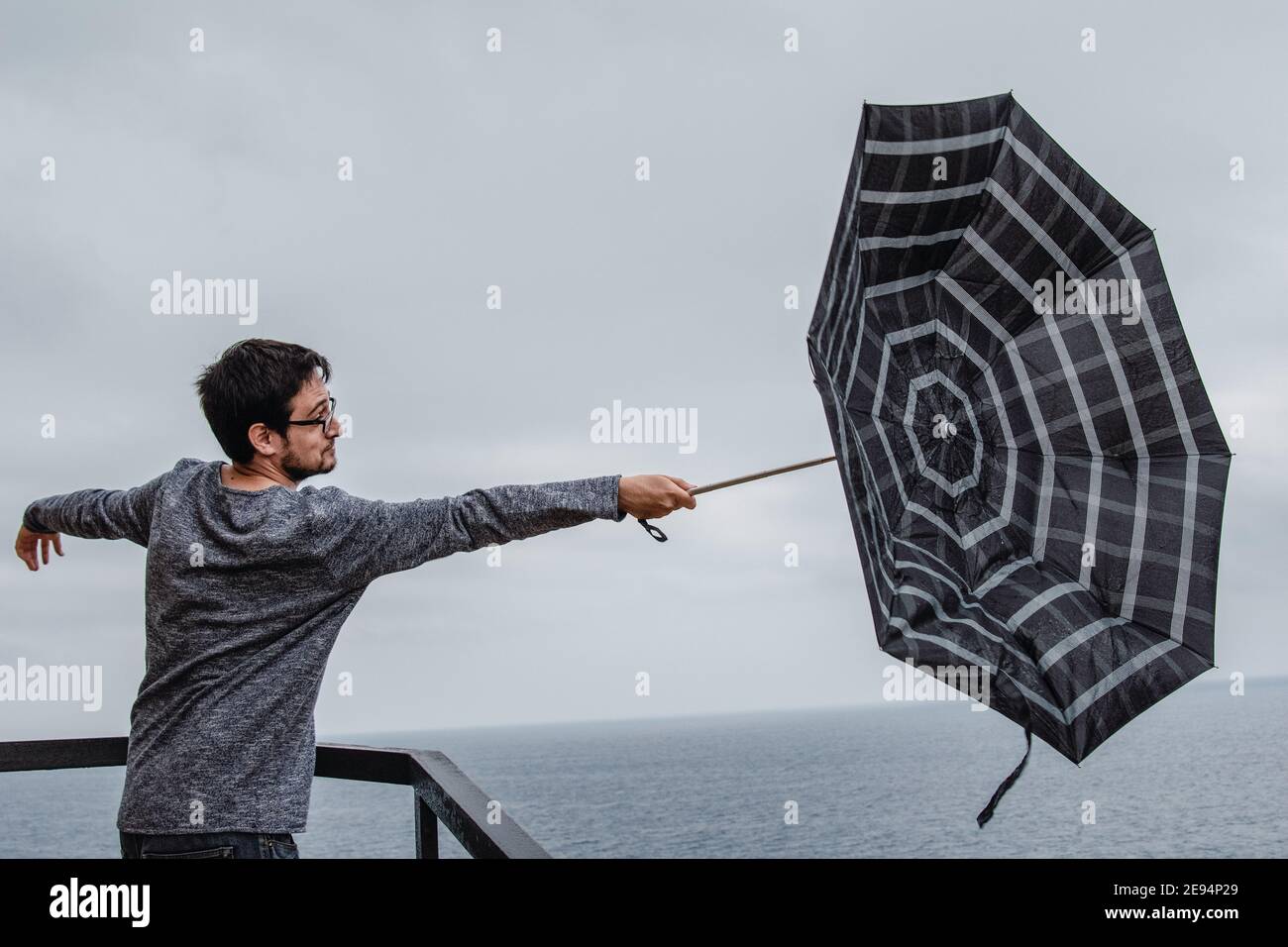 Giovane uomo con un ombrello girato dal vento Foto Stock