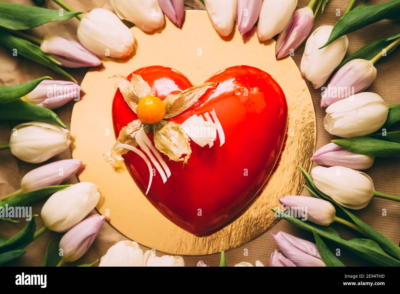 Torta rossa a forma di cuore per San Valentino, Festa della mamma, torta di compleanno con tulipani rosa. Fiori e torta a forma di cuore su sfondo oro in piano Foto Stock