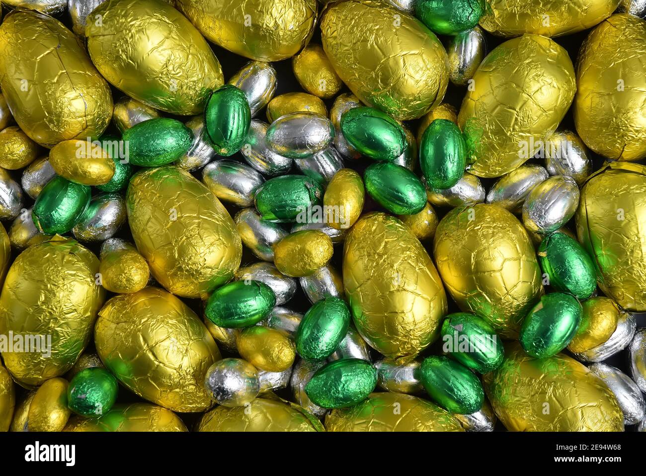 Grandi e piccoli colori giallo, oro, verde e argento primavera di cioccolato avvolto in foglio uova di pasqua, su uno sfondo nero. Foto Stock