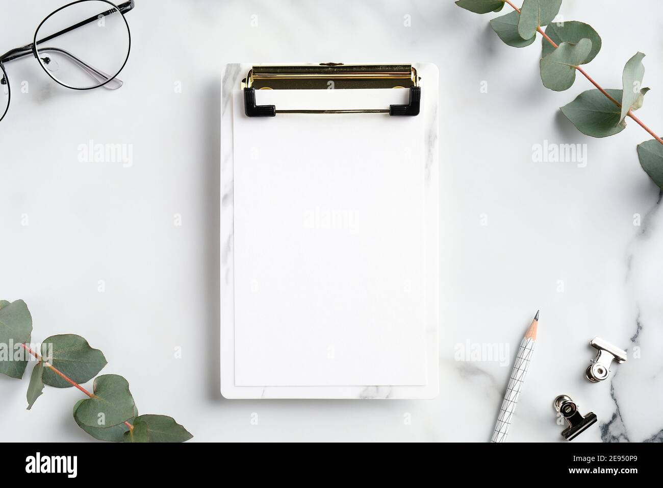 Elegante spazio di lavoro femminile con mokup di appunti, bicchieri, forniture per ufficio, rami di eucalipto su sfondo marmoreo. Disposizione piatta, vista dall'alto. Foto Stock