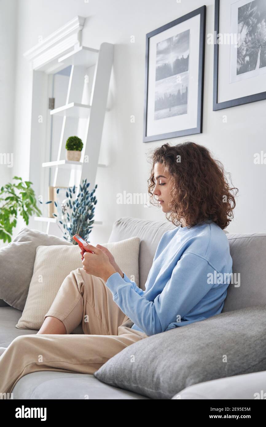 Ragazza teen che tiene il telefono delle cellule usando lo smartphone seduto sul divano a casa. Foto Stock