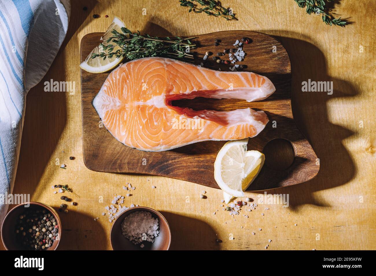 Bistecca di salmone crudo con limone e timo su tavola di legno, vista dall'alto. Illuminazione difficile Foto Stock