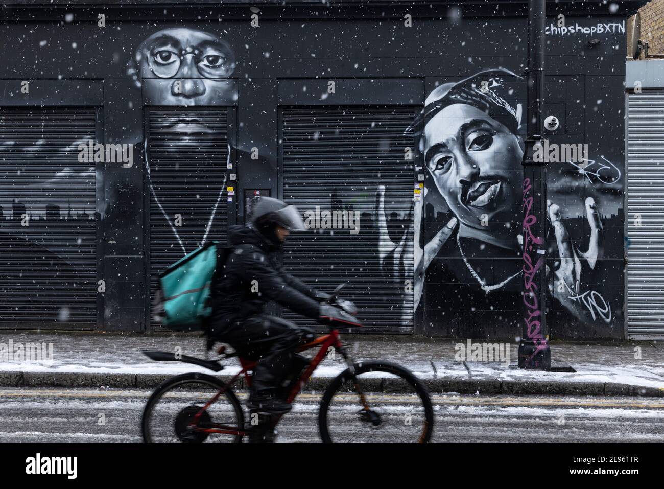 Un pilota di deliveroo passa attraverso murali di strada di rapper 'Big L' e '2Pac' durante la neve pesante, Atlantic Road, Brixton, Londra, 24 gennaio 2021 Foto Stock