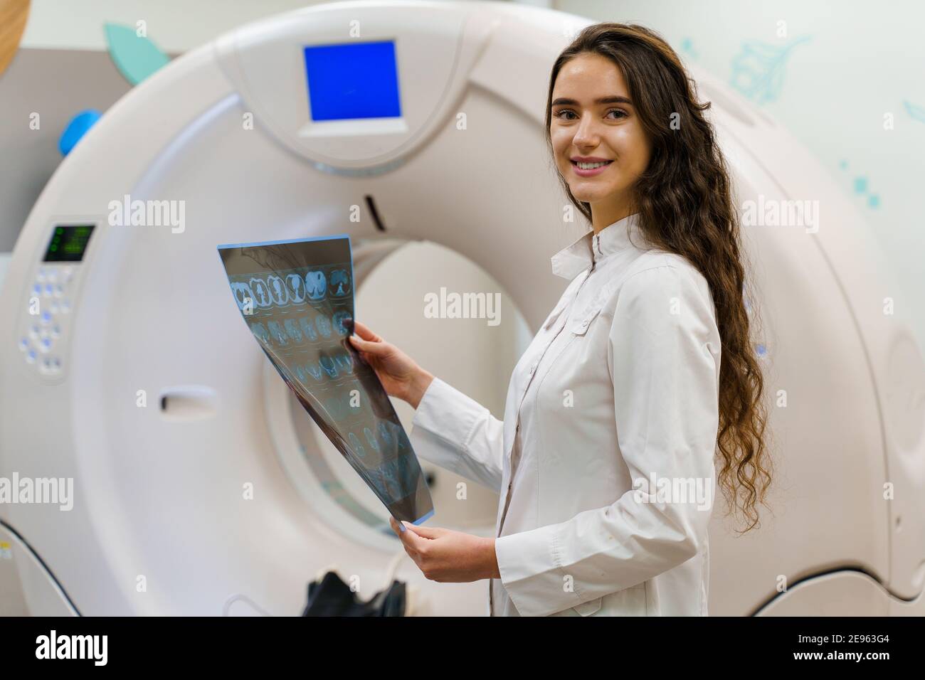 Lo studente medico guarda in macchina fotografica e sorride. Stand medici con immagine radiografica del cervello paziente nelle mani. La donna rimane di fronte a kt komputer tomogr Foto Stock