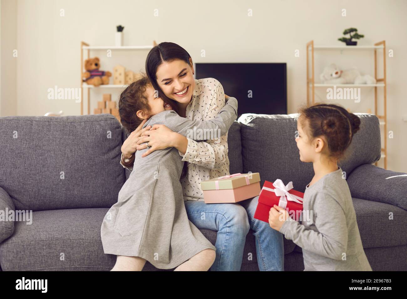 Felice giovane donna abbracciando i suoi figli e ringraziandoli per Regali il giorno della mamma Foto Stock