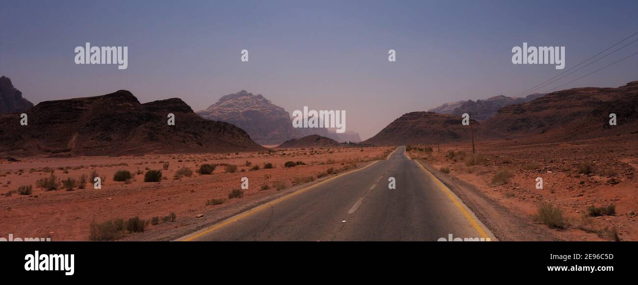 Lunga strada deserta con le montagne di Wadi Rum in lo sfondo Foto Stock